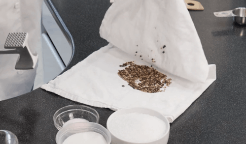 Ground coffee spilled on a white napkin on a dark kitchen counter, with cups of milk and sugar nearby.