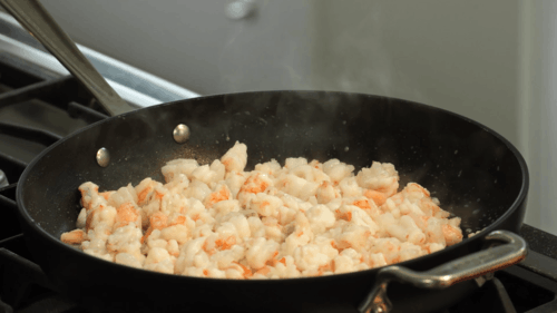 Diced chicken cooking in a black skillet on a stove, steam rising from the pan.