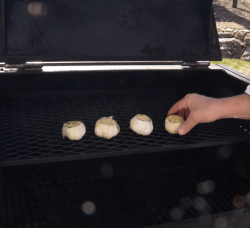 Person grilling four mushrooms on a barbecue, lining them up on the grate under an open lid.