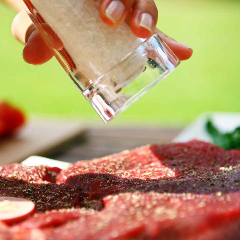 person adding salt to a steak